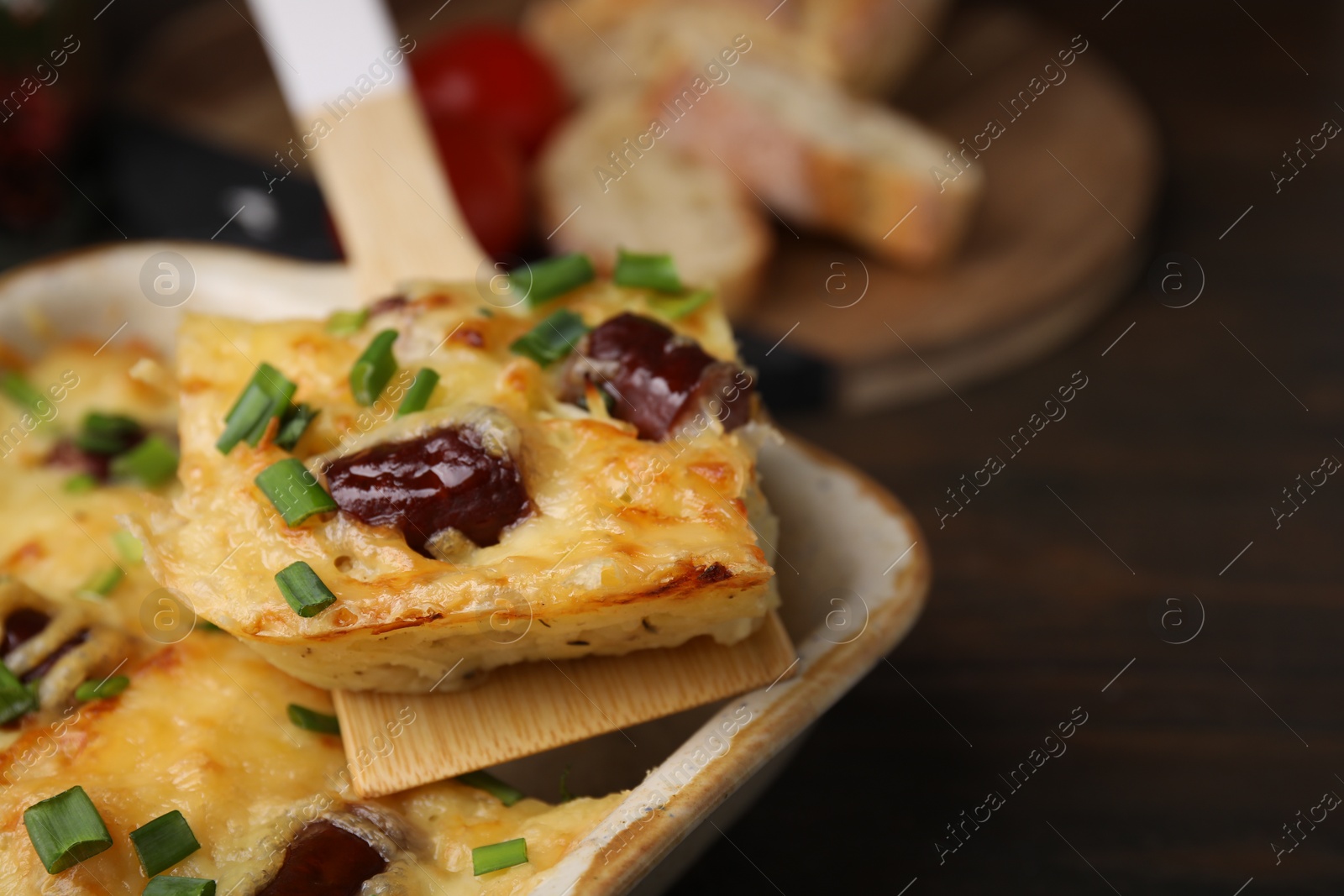 Photo of Taking piece of tasty sausage casserole from baking dish at table, closeup. Space for text