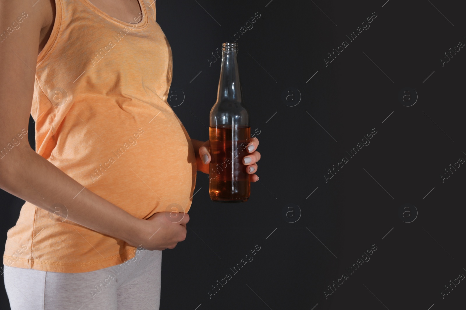 Photo of Future mother with bottle of alcohol drink on black background, closeup. Bad habits during pregnancy