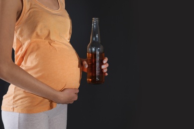 Photo of Future mother with bottle of alcohol drink on black background, closeup. Bad habits during pregnancy