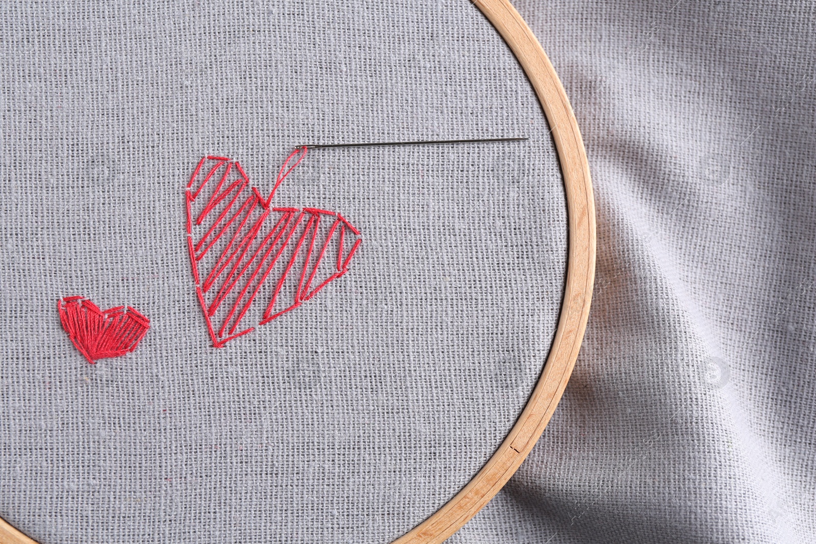 Photo of Embroidered red hearts and needle on light grey cloth, top view