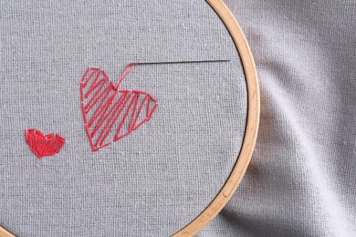 Embroidered red hearts and needle on light grey cloth, top view