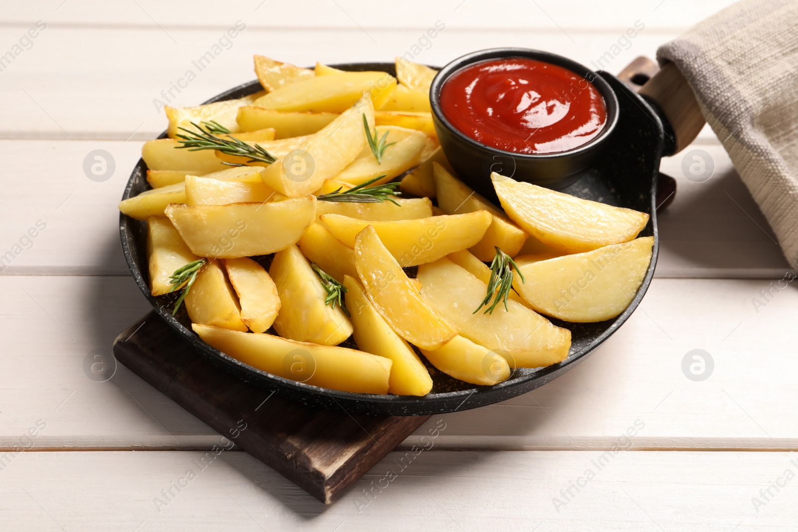 Photo of Pan with tasty baked potato wedges, rosemary and sauce on white wooden table