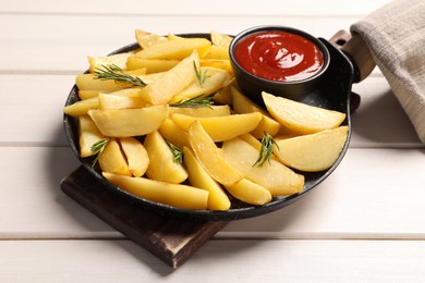 Photo of Pan with tasty baked potato wedges, rosemary and sauce on white wooden table