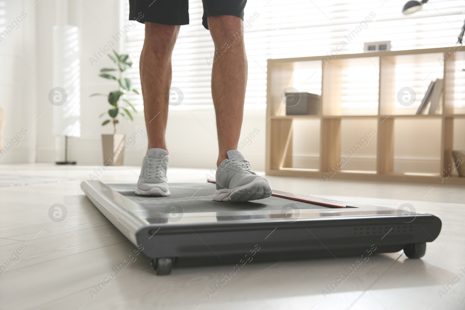 Photo of Sporty man training on walking treadmill at home, closeup