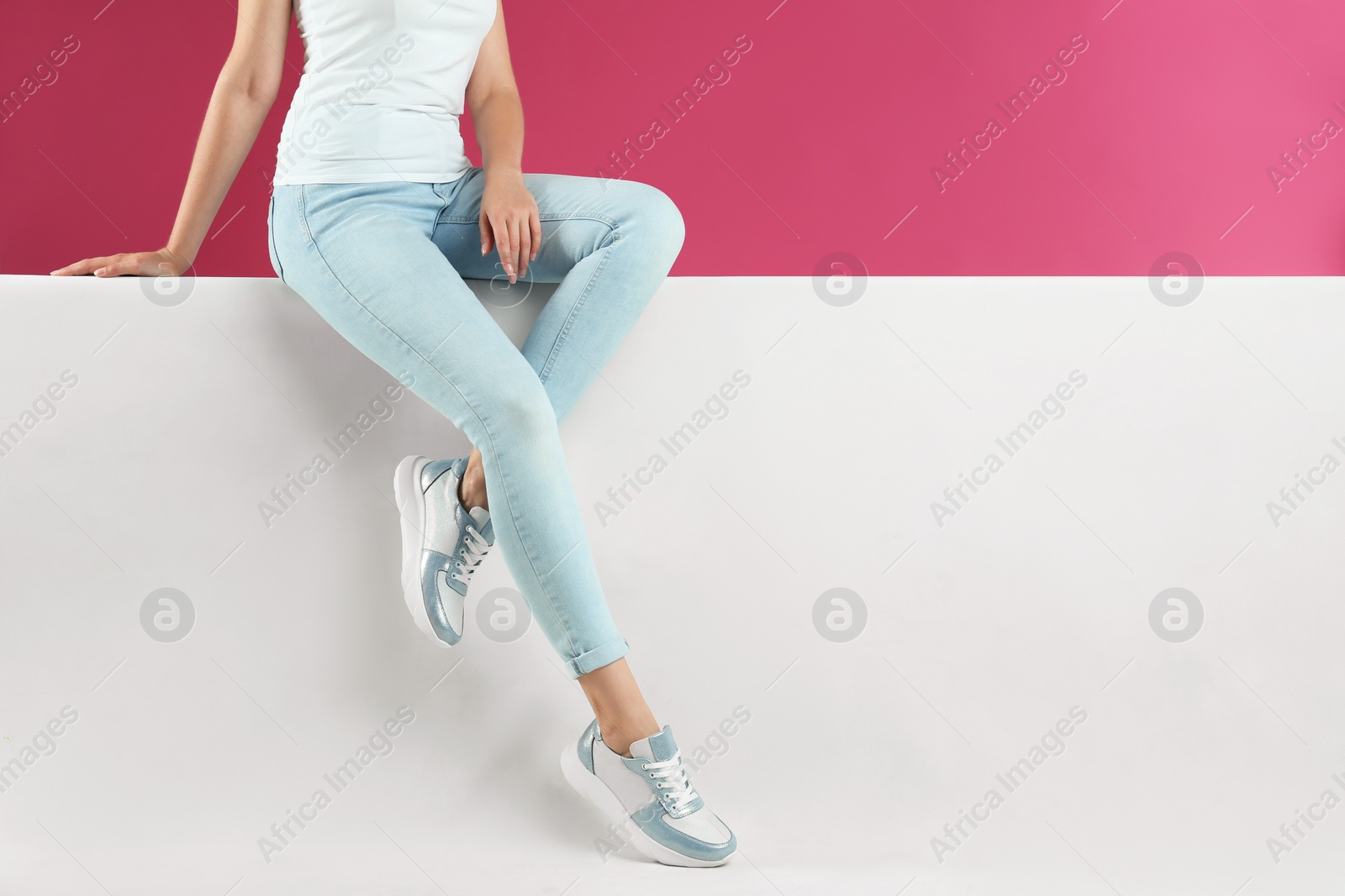 Photo of Woman in stylish sneakers sitting on color background, closeup