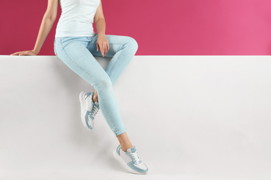 Woman in stylish sneakers sitting on color background, closeup