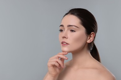 Young woman massaging her face on grey background. Space for text