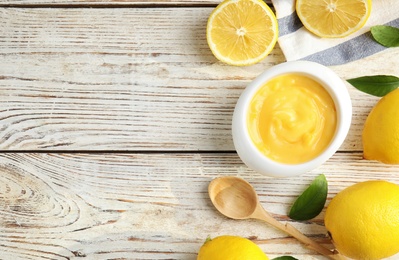 Delicious lemon curd in bowl on white wooden table, flat lay. Space for text