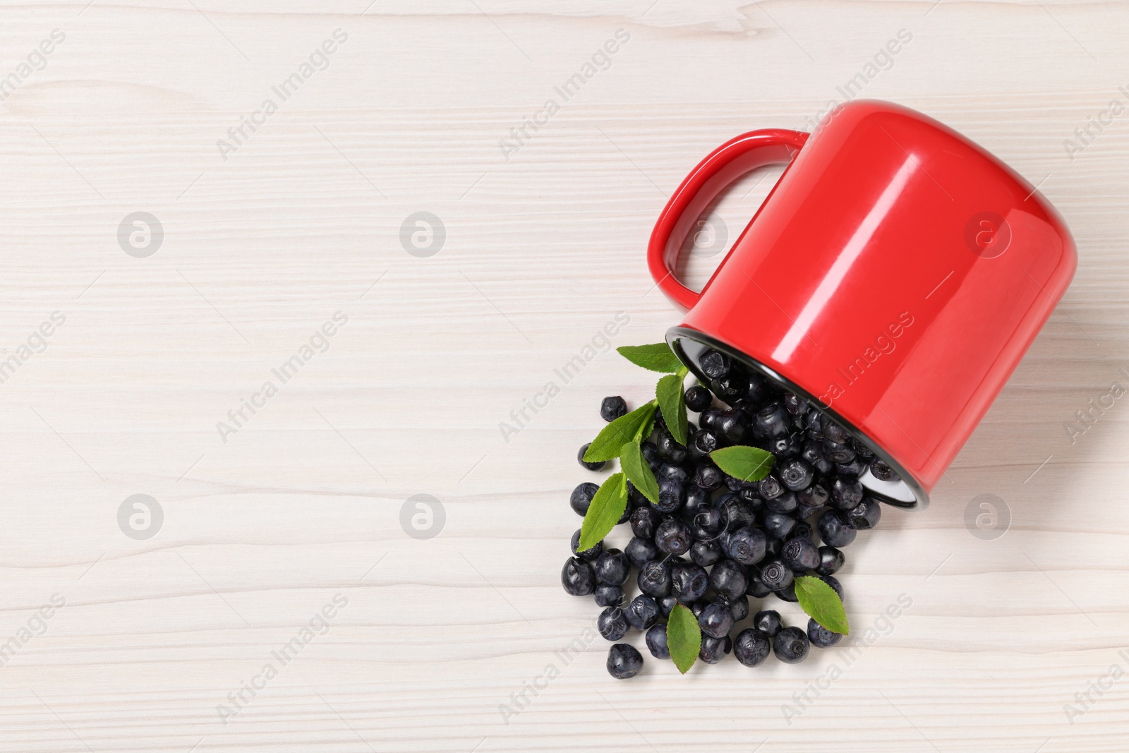 Photo of Mug with ripe bilberries on white wooden table, flat lay. Space for text