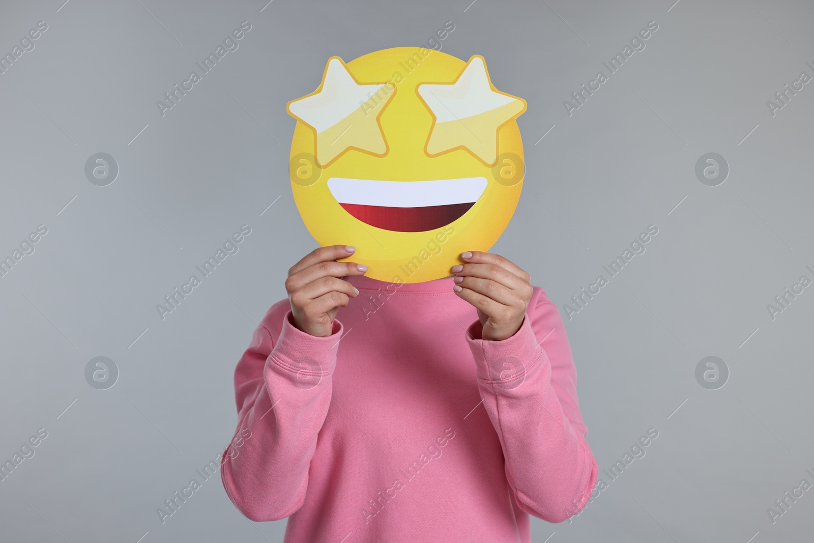 Photo of Woman holding emoticon with stars instead of eyes on grey background