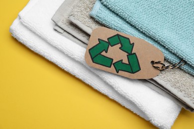 Photo of Stacked towels with recycling label on yellow background, closeup