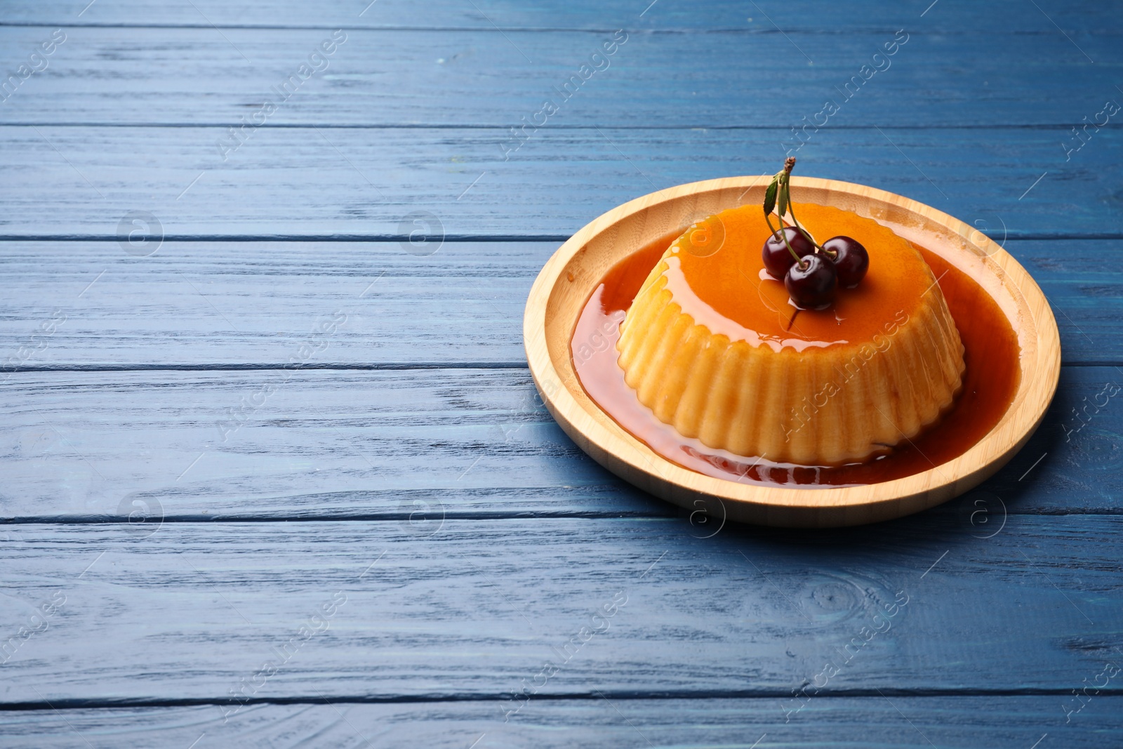 Photo of Delicious pudding with caramel and cherries on blue wooden table. Space for text