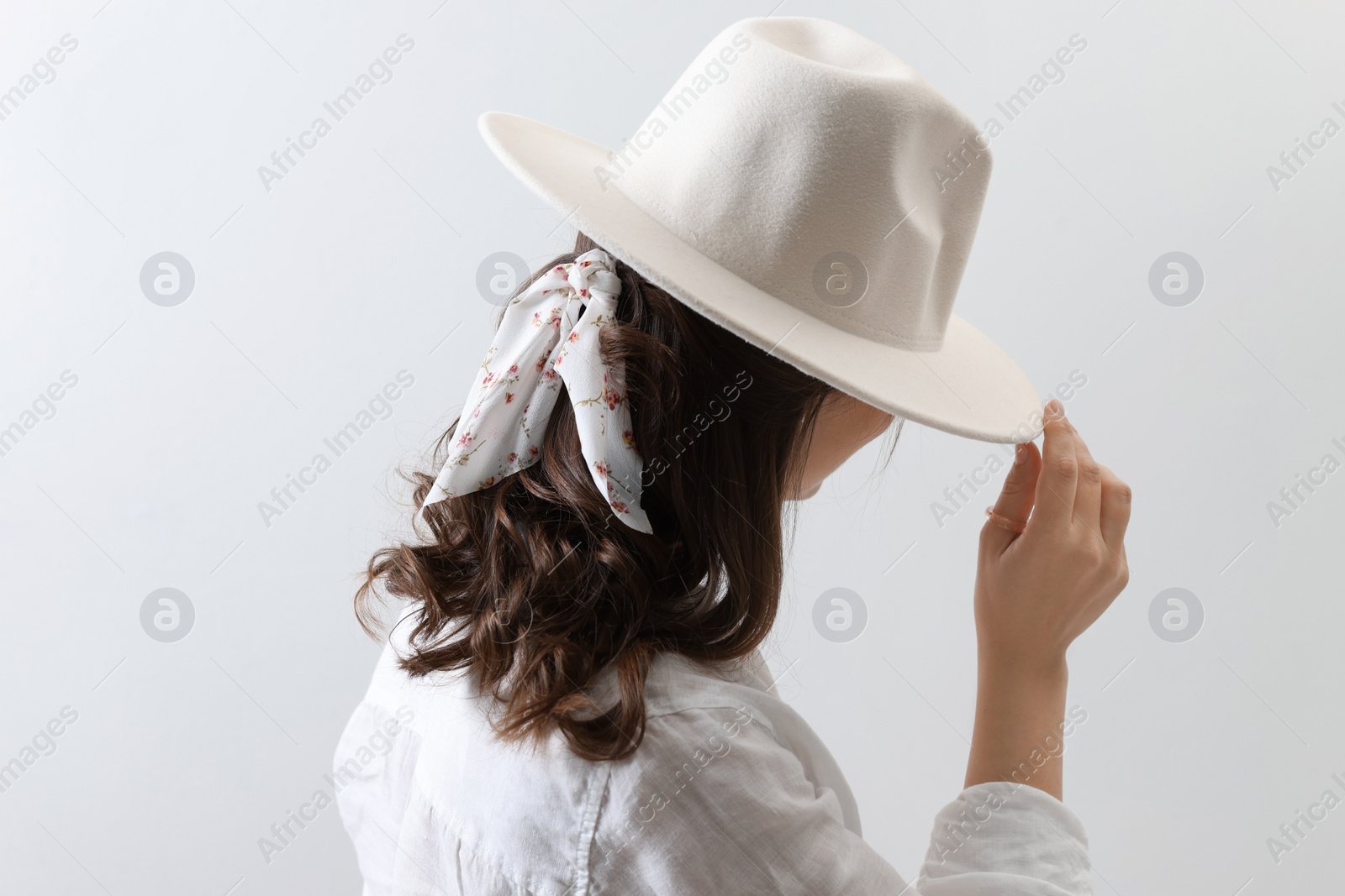 Photo of Young woman with hat and stylish bandana on light background, back view