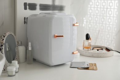 Photo of Cosmetics refrigerator and skin care products on white table indoors