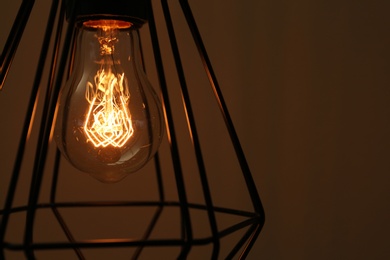 Hanging lamp bulb in chandelier against brown background, closeup