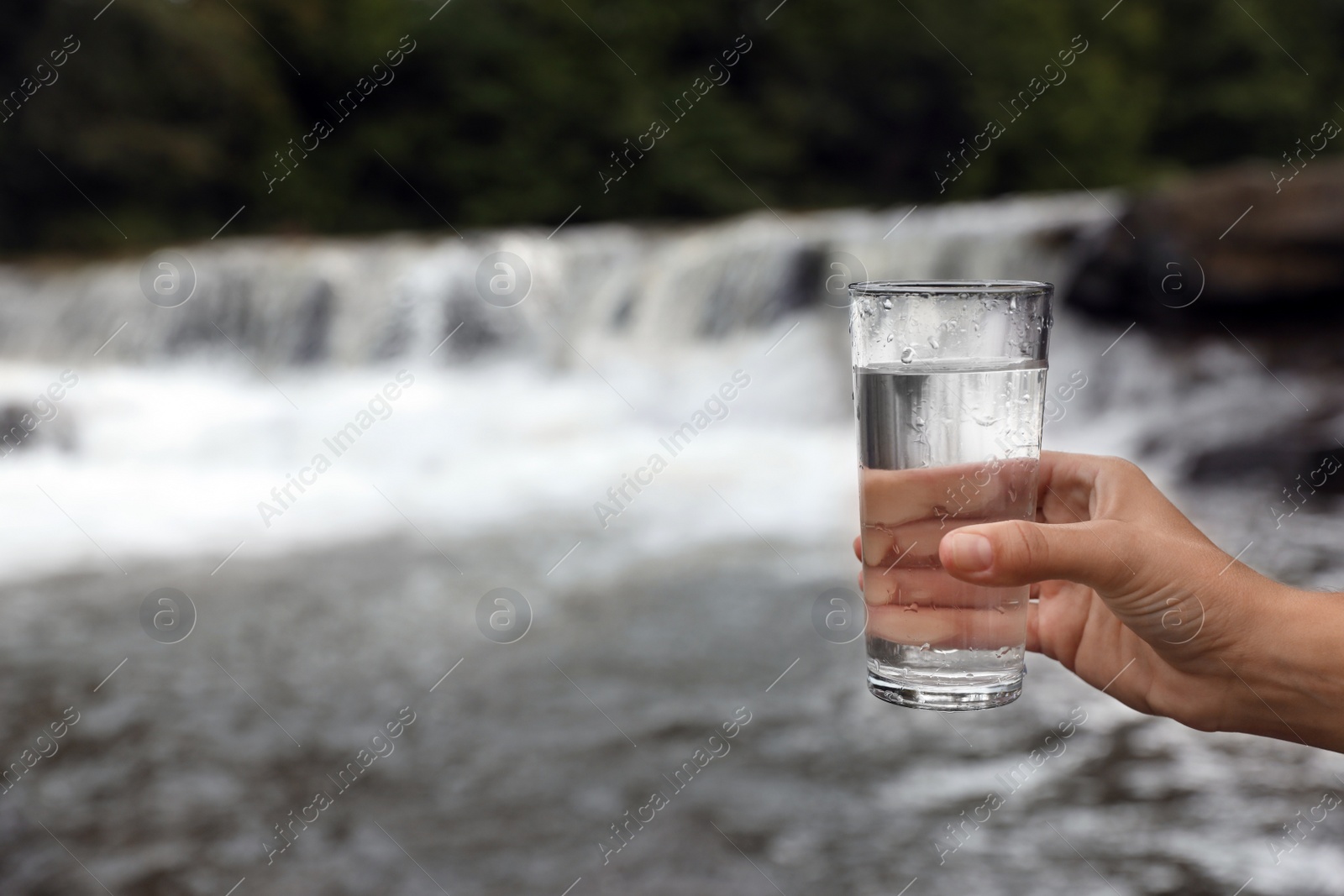 Photo of Woman holding glass of fresh water near river, closeup. Space for text