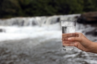 Woman holding glass of fresh water near river, closeup. Space for text