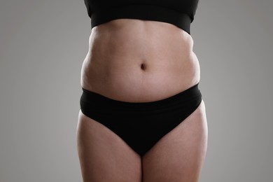 Woman with excessive belly fat on grey background, closeup. Overweight problem