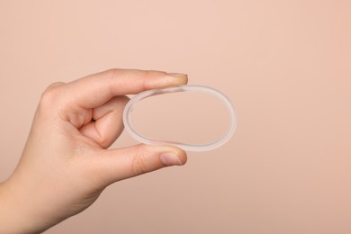 Photo of Woman holding diaphragm vaginal contraceptive ring on beige background, closeup. Space for text