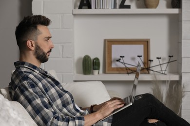 Man working with laptop in living room, space for text