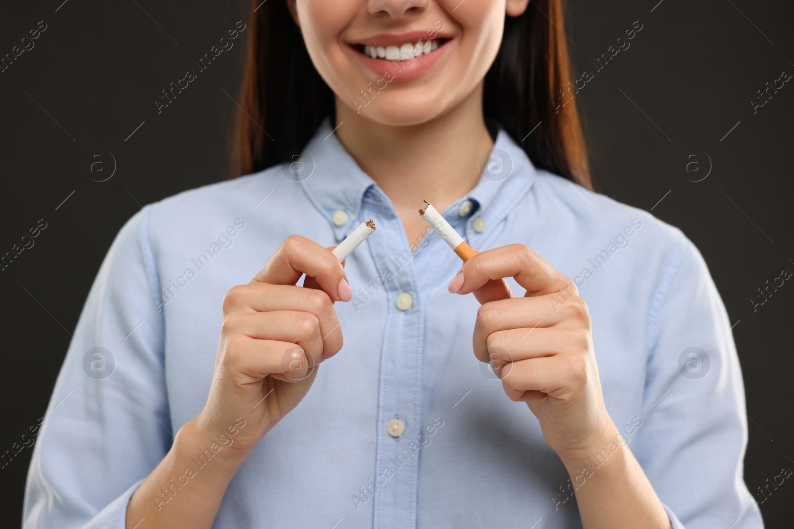 Photo of Stop smoking concept. Happy woman breaking cigarette on black background, closeup