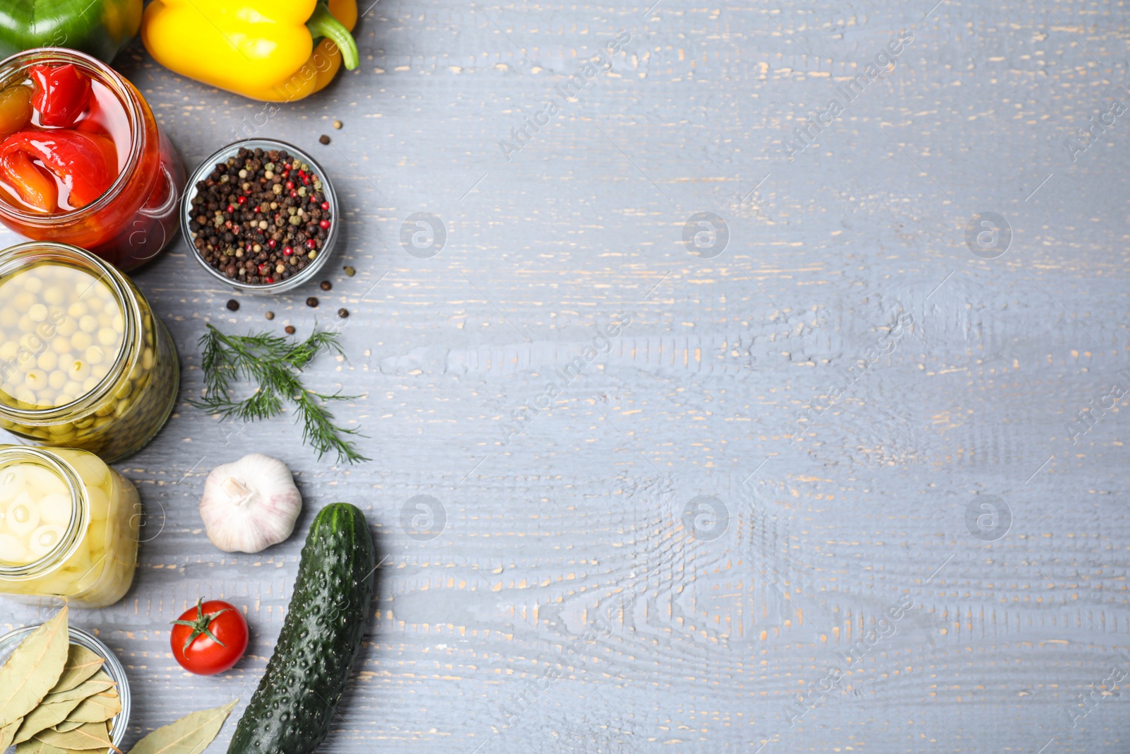 Photo of Glass jars with different pickled vegetables on grey wooden table, flat lay. Space for text