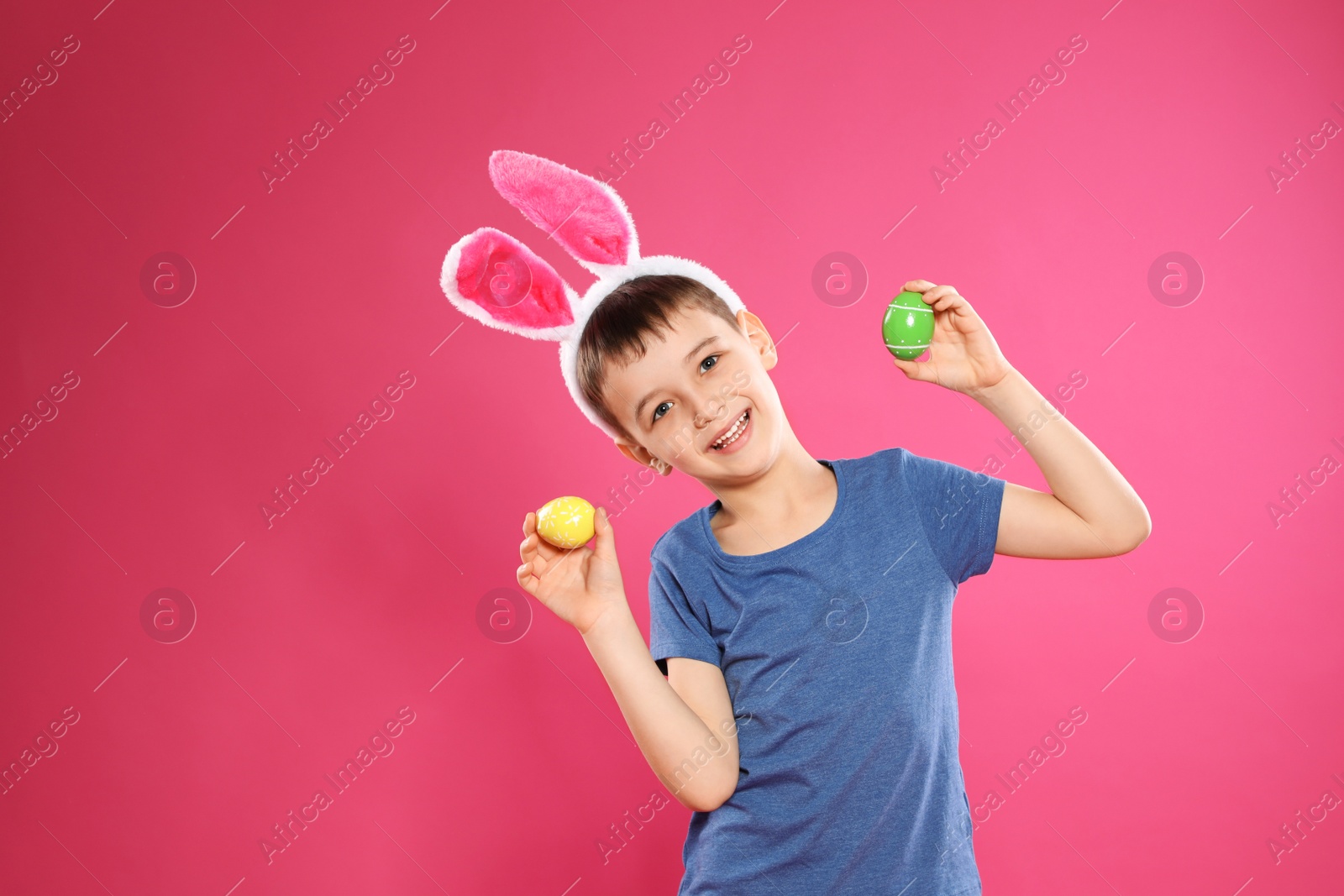 Photo of Little boy in bunny ears headband holding Easter eggs on color background, space for text