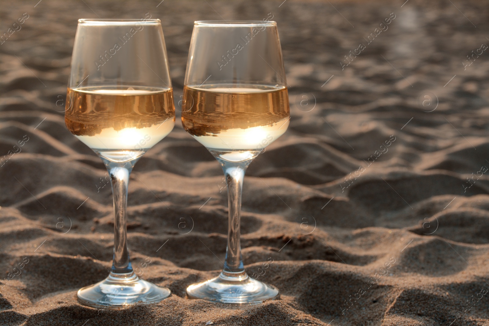 Photo of Glasses of tasty wine on sand, space for text