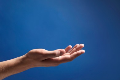 Man holding something in hand on blue background, closeup. Space for text