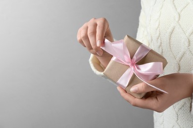 Photo of Woman holding gift box with pink bow on light grey background, closeup. Space for text