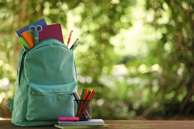 Color backpack and school stationery on table against blurred background, space for text