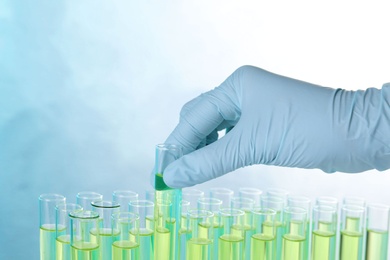 Scientist taking test tube with liquid sample on color background, closeup