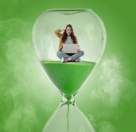 Worried woman with laptop sitting inside hourglass on green background. Flowing sand symbolizing coming deadline