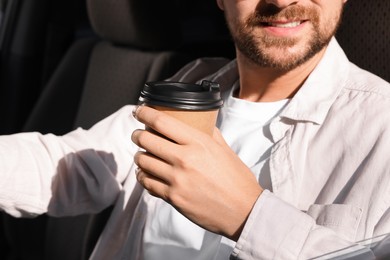 Photo of Coffee to go. Man with paper cup of drink in car, closeup