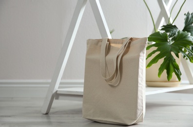 Photo of Eco bag and houseplant near white wall indoors. Space for design
