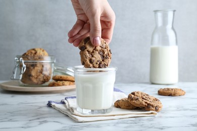 Photo of Woman dipping tasty chocolate chip cookie into glass of milk at white marble table, closeup
