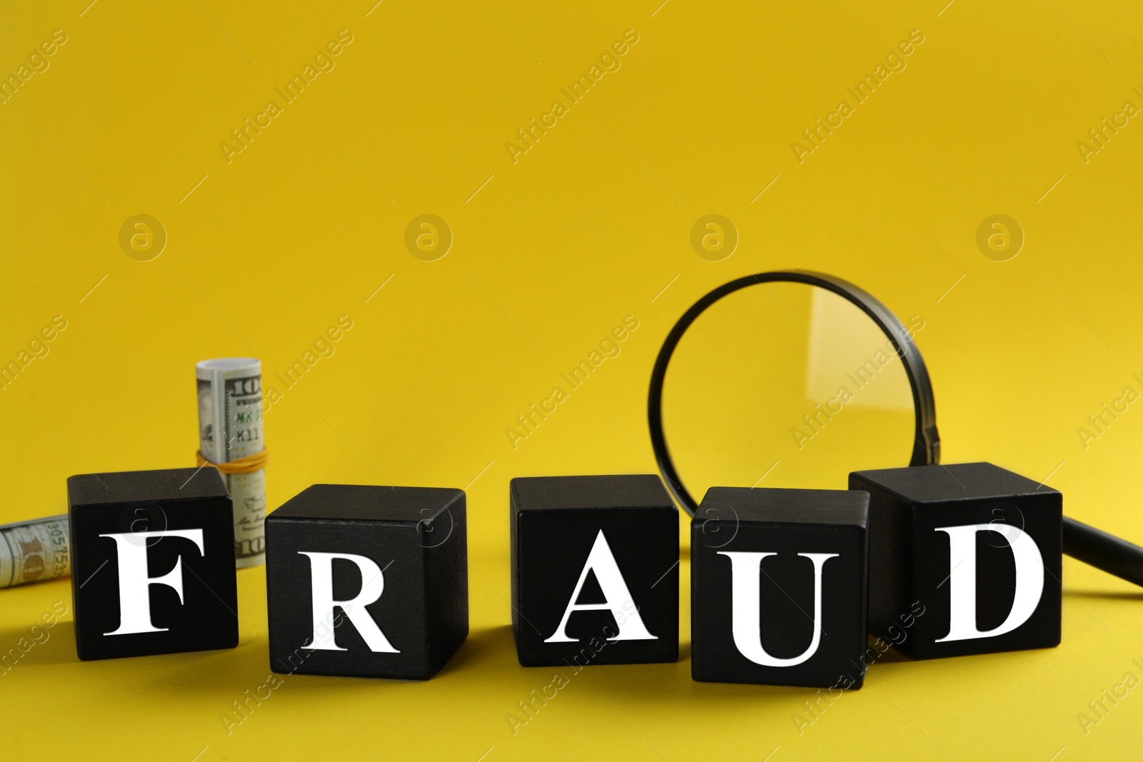 Photo of Black cubes with word Fraud, magnifying glass and money on yellow background, space for text
