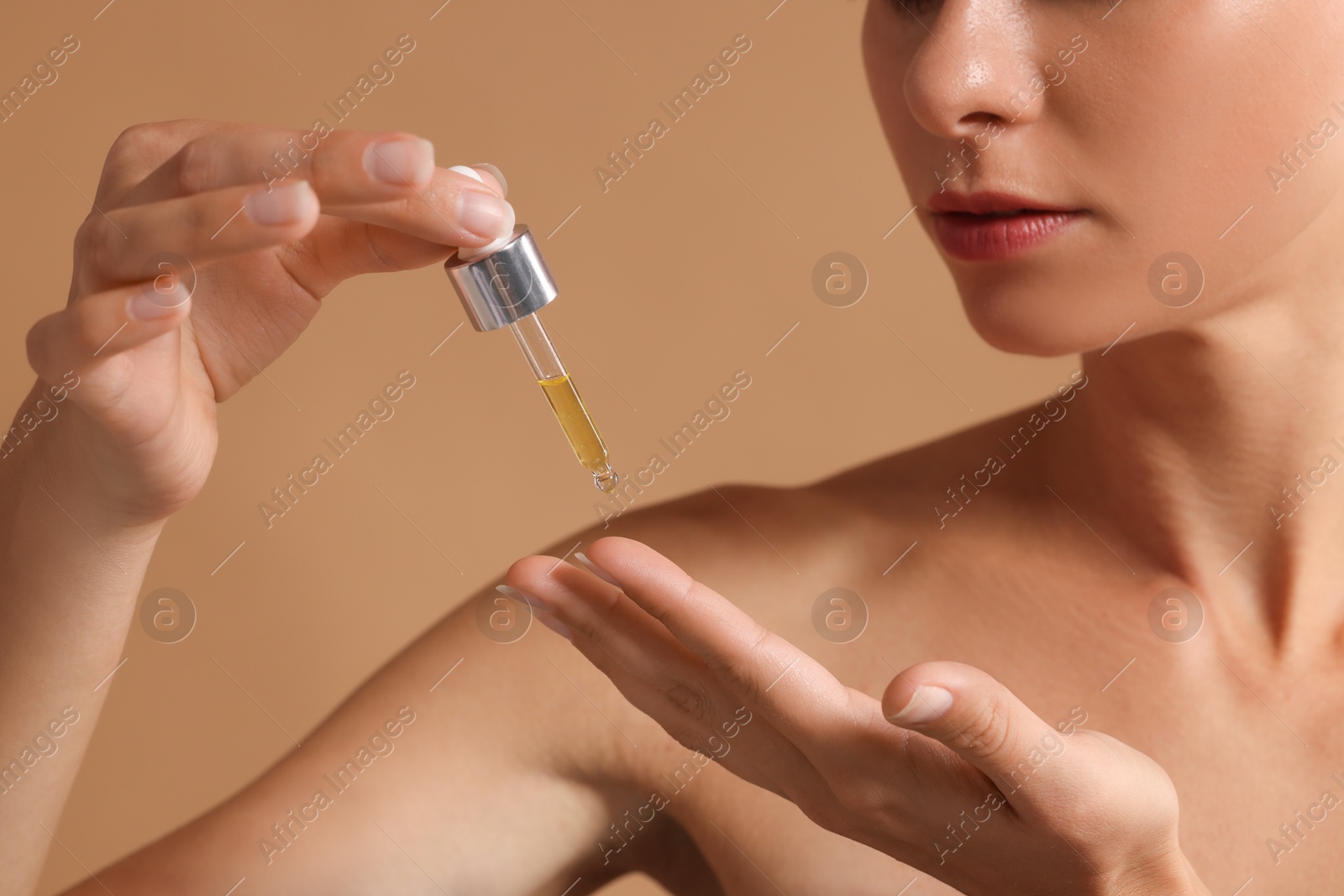 Photo of Woman applying cosmetic serum onto her hand on beige background, closeup