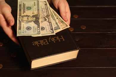 Photo of Donate and give concept. Woman with dollar banknotes, coins and Bible at wooden table, closeup