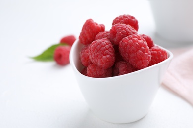 Photo of Delicious fresh ripe raspberries in bowl on white table, closeup