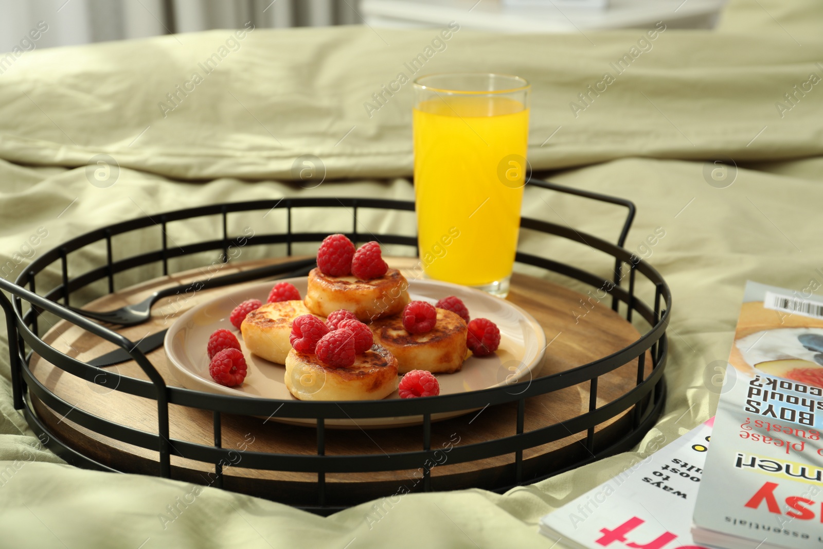 Photo of Tasty breakfast served in bedroom. Cottage cheese pancakes with fresh raspberries and juice on tray