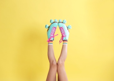 Young woman with retro roller skates on color background, closeup