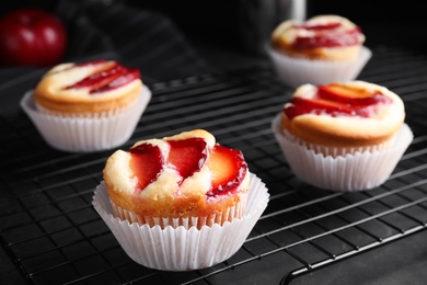 Photo of Delicious cupcakes with plums on black cooling tray, closeup