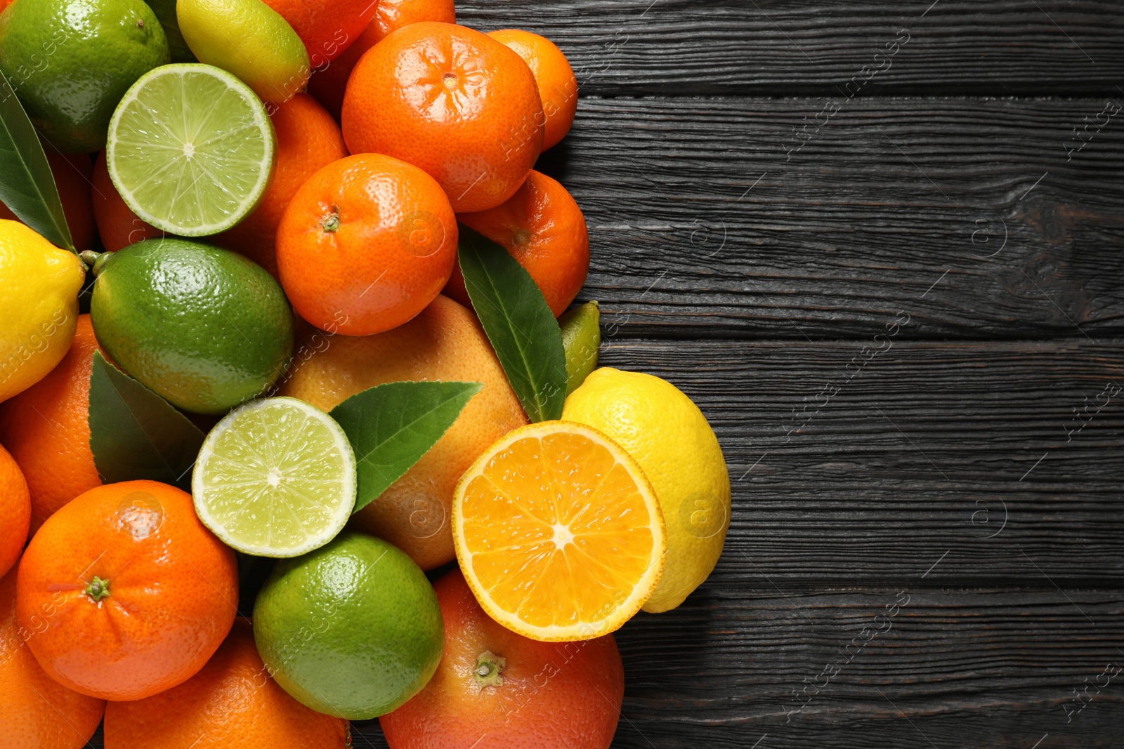 Photo of Different citrus fruits with leaves on wooden background, top view. Space for text