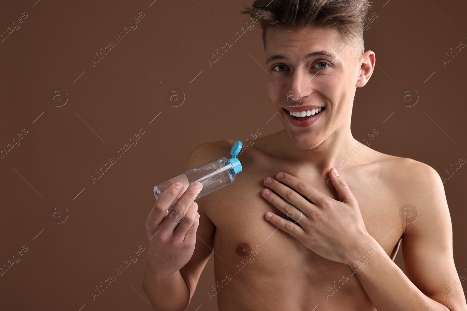 Photo of Handsome man applying lotion onto his body on brown background. Space for text