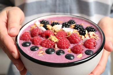 Photo of Woman holding bowl with tasty acai smoothie and berries, closeup