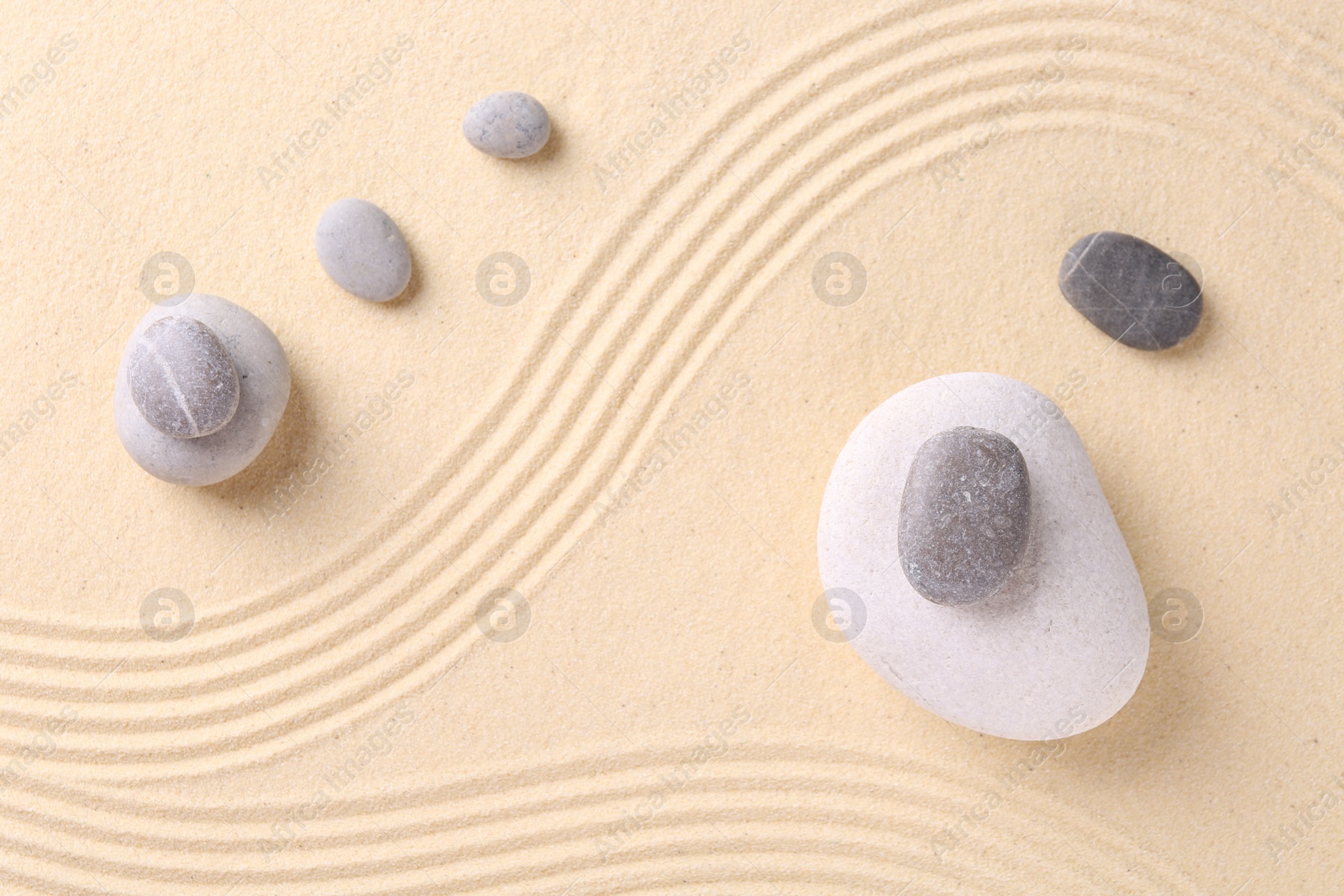 Photo of Zen garden stones on sand with pattern, flat lay