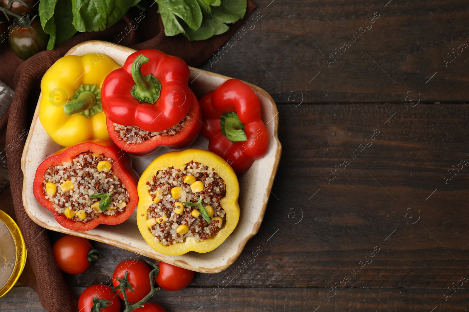 Photo of Quinoa stuffed bell peppers in baking dish, basil and tomatoes on wooden table, flat lay. Space for text