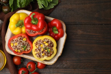 Photo of Quinoa stuffed bell peppers in baking dish, basil and tomatoes on wooden table, flat lay. Space for text