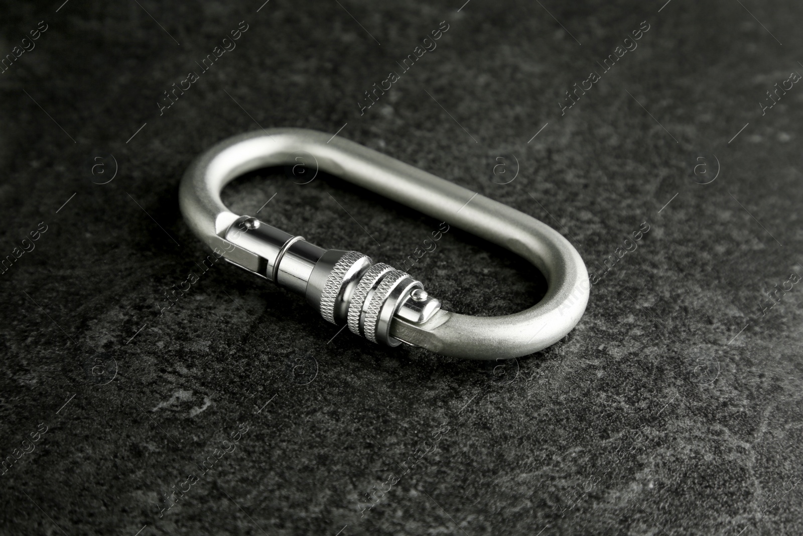 Photo of One metal carabiner on black table. Safety equipment